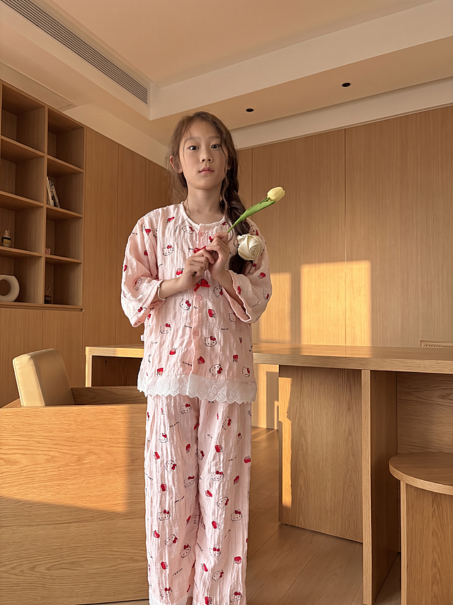 参考第一张图的暖色调家居风格和光影效果，将这张图片的背景替换为温馨简约的原木家居场景，保持女孩和粉色Kitty猫睡衣不变，制作成清晰的拼多多商品主图，暖光氛围感，高清质感