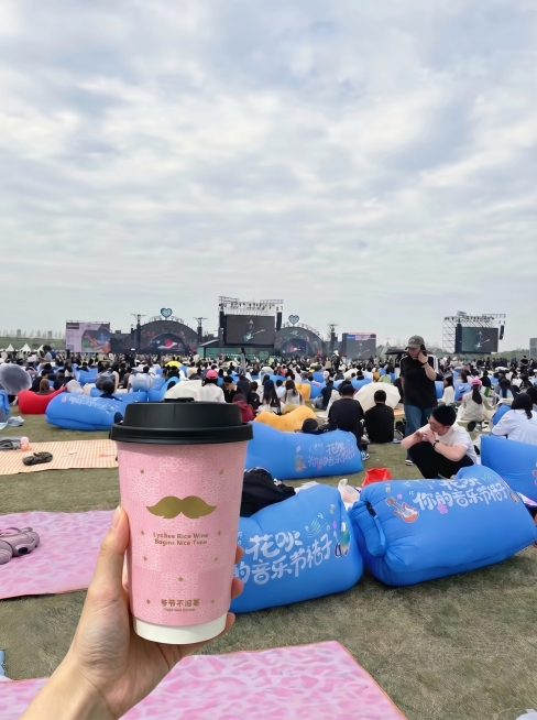 将粉色奶茶杯放到前景位置，以音乐节草坪背景图为整体场景，自然合成，保持真实光影和透视效果预览效果