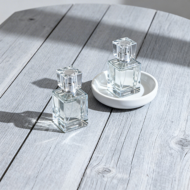 电商主图，2个极简设计玻璃香水瓶组合摆放在浅灰色木纹桌上，搭配白色陶瓷小托盘，冷调简约光影，水生调清新风格，画面无文字，突出香水瓶，正方形构图。