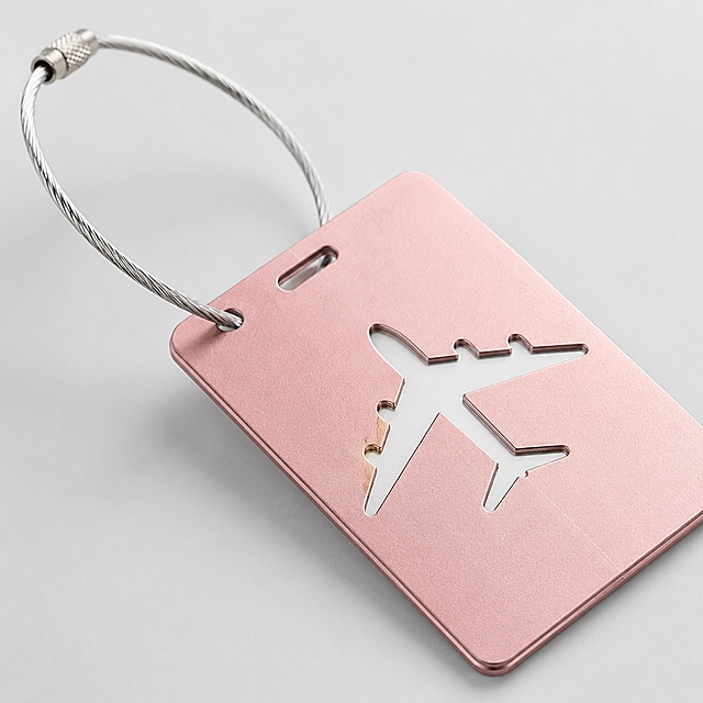 [Image 3] Detail close-up of metal luggage tag. Keep the product appearance, physical structure, material texture, color exactly the same as the input image, no any distortion or color difference. Do not include any trademarks or Chinese text. Close-up on airplane cutout shape and metal wire loop, highlight smooth metal edges, fine hollow craftsmanship, polished surface. Light gray background, soft side backlight to highlight metallic texture. 1:1 square composition, 2k resolution. Negative prompt: deformation, distorted text, blurred product, messy background, watermark, logo, Chinese text, black background.