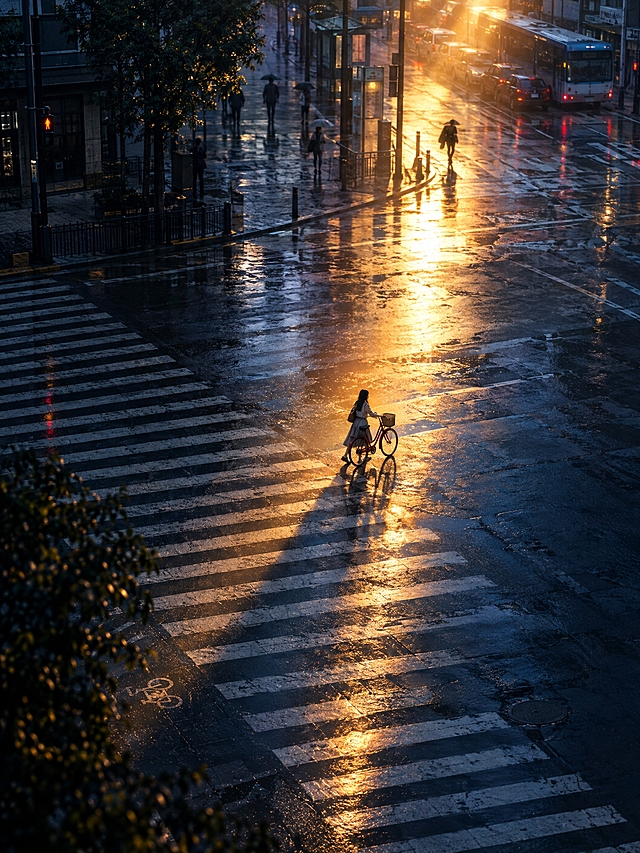 竖版电影静帧，3:4。黄昏雨后的城市十字路口，从高处俯视宽阔的斑马线，一束琥珀色阳光斜照在湿润路面上；一位年轻东亚女性推着红色自行车穿过光束，远处有模糊行人与停靠车辆。深蓝阴影与暖金反光强烈对比，人物很小，画面安静、孤独、真实电影摄影。画面中无文字、无logo、无水印、无字幕。超高清2K画质，细节丰富。