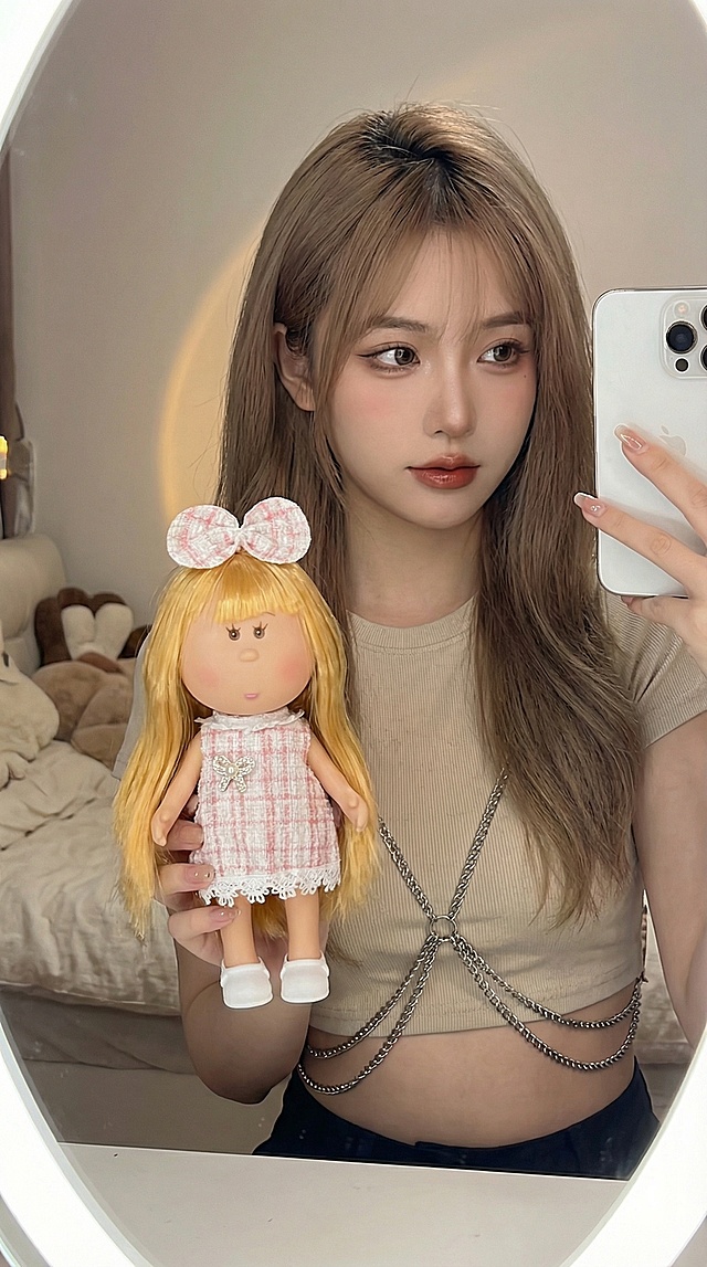 图中的娃娃高度在24cm，需要生成奶茶发色美女，拿着娃娃，对镜子自拍的照片。要求9：16，画质高清，手中娃娃清晰，人物只露出上半身，美女风格可以多元化，比如御姐，辣妹，甜妹等，适合小红书平台种草娃娃产品的照片，生成不同的10张照片。