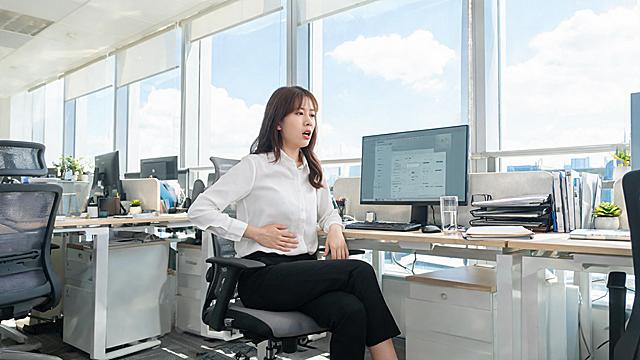 全景，明亮自然光，年轻白领女生坐在办公桌前，对着电脑叹气，手摸自己的小肚子