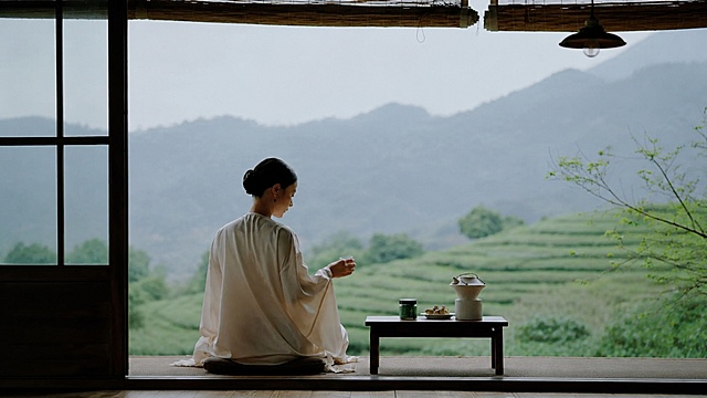 参考原图的禅意茶文化风格，调整为横图，保留原画面元素：穿素色白衣的女子背身静坐，窗前茶桌摆放茶具和茶点，背景是茶山和远山，保留日式禅意和氛围感