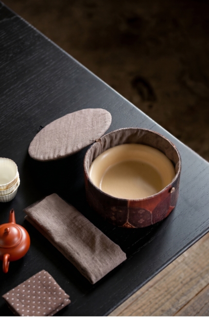 将图一茶事包的灰色内衬和左边的灰色长条布换成图二的浅棕色亚麻材质，保持包内的米黄色陶瓷盘子不变，保持原图片的构图、光影和画质清晰预览效果