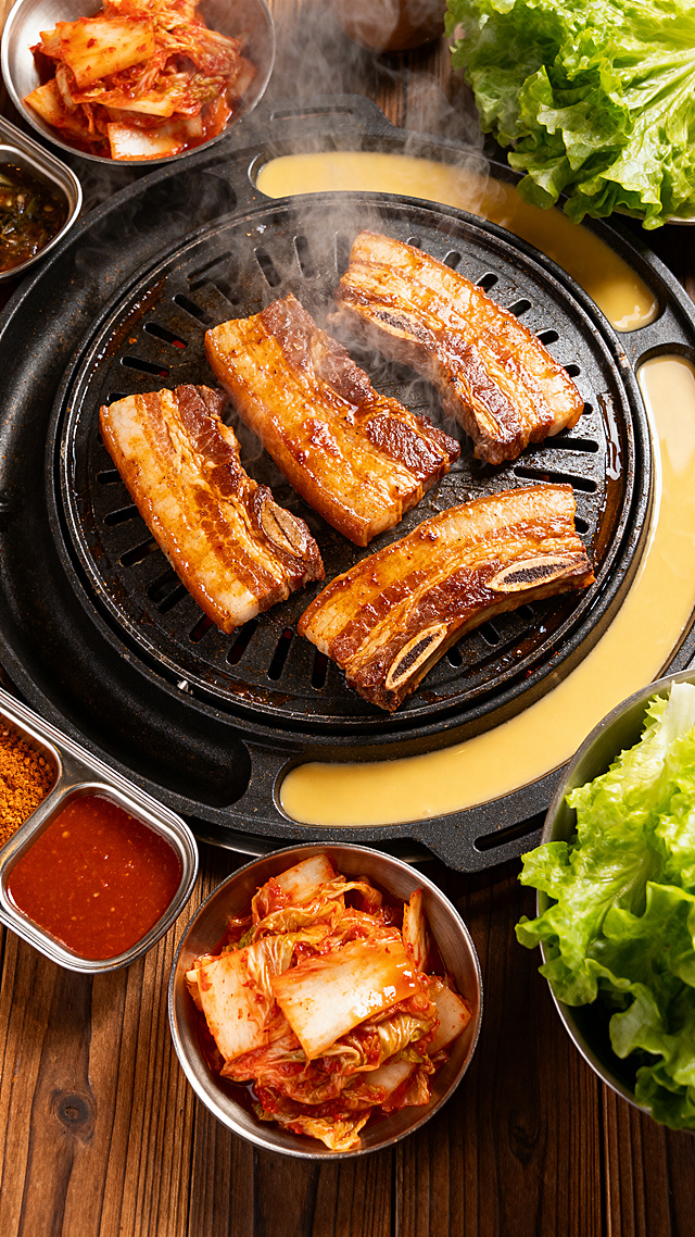 重新生成滋滋作响的韩式烤肉，烤盘上摆放着腌制好的五花肉、牛肋条，肉片油花丰盈，周围搭配韩式泡菜、生菜、酱料，色调温暖诱人，更具食欲感，4K高清美食摄影