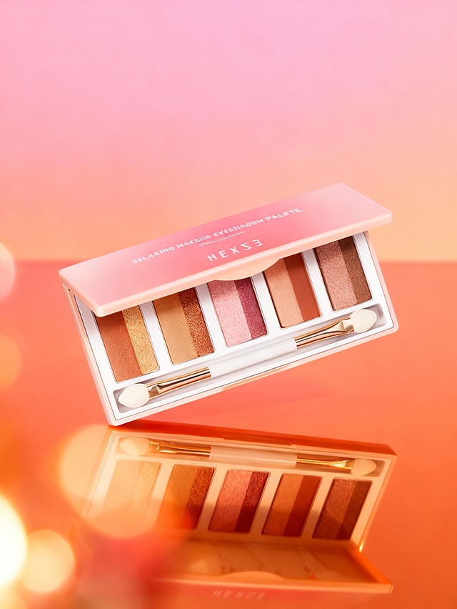 奢华暖调的商业摄影风格，高质感精致渲染；画面采用粉橙渐变的浓郁暖色调，整体氛围高级且富有视觉吸引力；以微俯近景视角、展示式构图呈现，视觉重心聚焦于主体的色彩与细节；场景包含粉橙渐变的柔和虚化背景、前景光效遮挡，高反光的暖色调台面（呈现产品清晰倒影）；主体呈倾斜角度摆放完整展示；暖调背景衬托主体浓郁色彩，高反光台面强化奢华质感，打开的布局突出主体细节；配合柔和定向光照明、浅景深效果、眼影珠光与哑光质感的细腻表现及暖色调的自然过渡