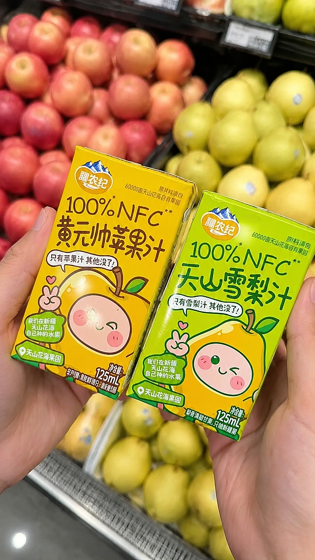 超写实商业产品摄影。
主体：两款果汁饮料盒（黄元帅苹果汁和天山雪梨汁）严格参照上传产品图，完整保留所有可见组件、轮廓、结构、比例、材质、颜色与产品本体上的文字信息，与上传图完全一致，依然被双手自然手持展示；更换背景为超市新鲜水果售卖区，保持产品和手为第一视觉焦点，自然融入场景光影，与场景共处同一物理空间。
构图：45度斜俯拍特写构图，两款产品并排展示，两个产品之间留有合理物理空间，无穿模和不合理遮挡。
风格：真实商业摄影，新鲜自然的生活氛围。
场景：超市生鲜水果区背景，摆放着新鲜的苹果和雪梨鲜果，色彩鲜艳自然。
空间：①产品主体在画面前景，保持双手握持的姿态；②背景是超市水果货架，摆放新鲜鲜果，模糊虚化处理突出主体；③背景无同类果汁产品。
配色/材质：画面明亮自然，超市冷白色灯光，水果色彩丰富鲜活，产品包装色彩鲜艳饱和，饮料盒为纸质包装。
光影：主光来自超市斜前方冷白光，照亮产品包装，清晰展示文字和图案，整体明亮自然，轻微环境反光，无生硬阴影。
严格锁定宽高比为 9:16。