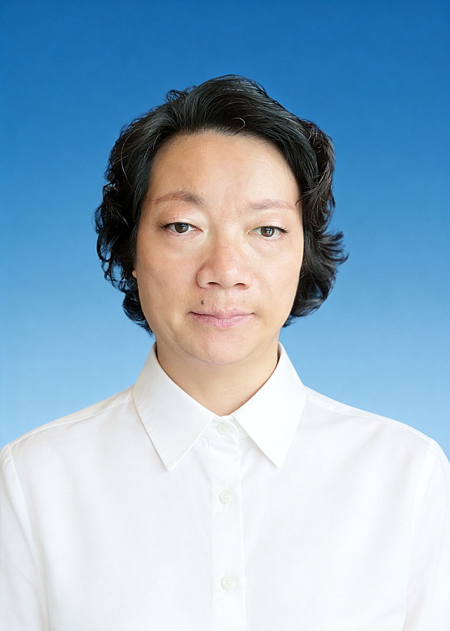 生成标准样式的证件照:参考第一张图保留人物脸型､年龄特征;参考第二张图的人物占位和比例;标准焦段50mm,纯正面胸像,提亮肤色,消除暗沉,轻度美颜,清透裸妆,隐形毛孔,均匀肤色,唇色自然提亮;头部发型完整,肤色白皙细腻,纯正面,头顶至上边缘有5%的距离,入境范围头部至胸部以上区域;人物居中,下巴距下边缘约30%,肩部平展,人物占比约画面的70%;均匀柔光,面部明亮无硬影,背景均匀提亮,画质清晰,零噪点降噪;表情自然柔和,嘴角微微上扬,面部清晰(脸部无遮挡);眼神澄澈看向镜头,淡妆,肤质白皙细腻;冷调白皙,极淡裸粉哑光眼影打底,极细内眼线填充睫毛根部,大直径深棕色带细微高光点的自然款美瞳;边缘模糊无生硬轮廓;唇面透亮润泽;身穿净白色翻领衬衫,白色纽扣,款式经典正式;均匀柔光,面部明暗过渡自然(无硬阴影､无高光反光点);面部亮度高于背景7%,突出人像主体;去除人物之外的所有元素,头部发型完整;纯净蓝色纯色背景(无任何杂物､纹理､渐变);背景亮度均匀统一(无明暗差异);高清锐利画质,细节清晰可见;零噪点处理(无颗粒感);色彩还原自然(无偏色),严格按照第一张图内容生成｡