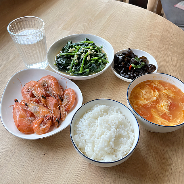 餐桌上的月子午餐，白米饭、清蒸虾、蒜蓉菠菜、番茄蛋花汤、一小碟凉拌木耳，用普通家用餐具盛装，桌子是浅色木质桌，旁边有一杯温水，自然光从侧面照入，食物新鲜有光泽，真实家常感，手机随手拍风格，不刻意摆盘
