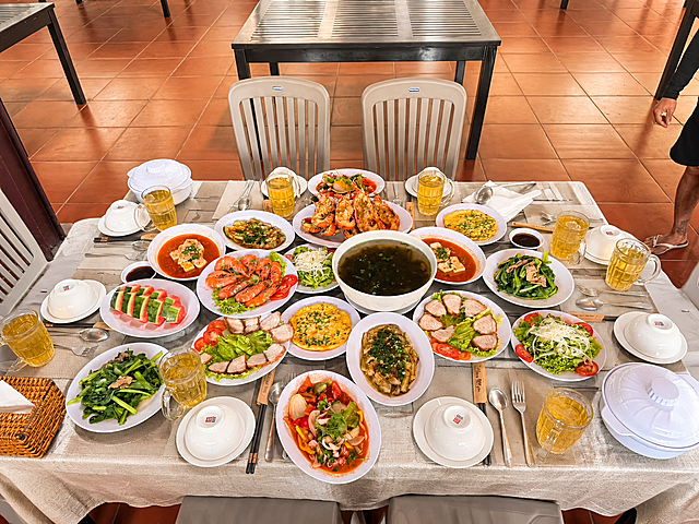 对这张美食餐桌照片进行美化，提升画面质感：增强食物的色泽饱和度和新鲜度，让菜品看起来更诱人；优化整体光线，使画面明亮通透、光影自然；提升图片清晰度和细节；在黑色桌面上增加一张精致的米白色棉麻质感桌布，桌布自然铺展，边缘有自然的褶皱垂感，与餐桌和菜品融合自然真实；整体色调温暖有食欲，保持俯拍视角和所有菜品、餐具的原有布局不变，画面真实自然，美食摄影风格
