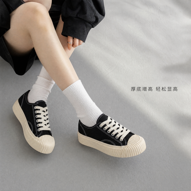 [主图-2] 跃步黑色帆布鞋上脚效果展示图。[氛围风格] 年轻活力街头松弛感；[画质] 商业摄影质感、光线柔和通透、产品清晰真实、画面干净高级。[元素] 年轻亚裔女生腿部出镜，交叉坐姿露出上脚的跃步黑预览效果