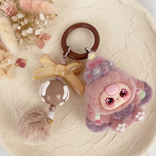 将这张毛绒挂件商品的背景换成奶油风ins风格，保持主体挂件商品结构和颜色完全不变，只更换背景。让商品居中放置，商品大小比例合适不要太小。背景为奶白色肌理感桌面，左上角点缀干燥花装饰，柔和自然光，光影温预览效果