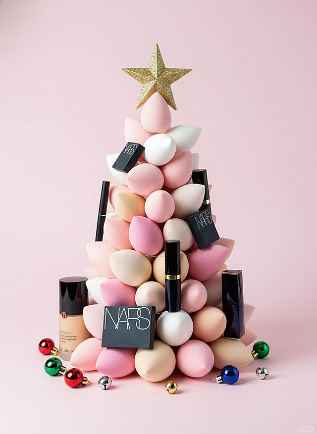 美妆蛋做的圣诞树造型，上点缀参考图的美妆产品，搭配星星、小铃铛等圣诞元素，但画面不要太杂乱，粉色背景。