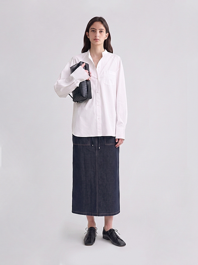 【主体保护指令】请保持参考图1中的【服装、穿着形态、构图】一致，包括服装款式/颜色/材质、合身度，不做改动。将模特的整体替换为参考图2模特的面部五官、发型、肤色、体型与气质特征。

修正要点：
1. 头部比例缩小，使头身比更协调自然，符合真实人体比例；
2. 右手持黑色鳄鱼纹手拿包，包上只有一只右手，去除多余的手，手部形态自然正常；
3. 去除所有手指甲的指甲油，指甲为自然健康的裸色状态，无任何彩色指甲油。

高端时尚商业摄影，极简高级质感，画面干净通透。

保留参考图1的原姿势：正面站立，右手持黑色鳄鱼纹手拿包于胸前，左手自然垂于身侧，双脚并拢站立，头部朝向与身体姿态完全与参考图1一致。整体替换为参考图2的女模特：深棕色中长发，自然微卷，发量柔顺有光泽；脸型偏椭圆，下颌线清晰柔和，五官立体深邃，眉骨与眼窝轮廓分明；深棕色眼眸，眼形偏长，眼尾微微上扬，睫毛自然纤长，眼妆干净清透；眉毛为自然野生眉，眉峰柔和，眉色与发色一致；鼻梁高挺线条流畅，鼻头精致；嘴唇厚度适中，唇形饱满，唇色自然裸粉，妆感清透；肤色为自然暖调白皙，肤质细腻光滑，带有自然的肌肤肌理与光泽；年龄约25岁左右，身形高挑纤细，身姿挺拔舒展；气质清冷高级，沉静内敛，专业模特表现力强，带有独特的文艺疏离感；表情平静自然，嘴角平直无笑意，面部肌肉放松；眼神沉稳坚定，正视镜头，传递出冷静自信的气质。新模特整体与原图背景、光影、构图自然融合，服装合身度保持不变，领口、袖口、裙摆处与身体自然贴合。头部比例协调自然，头身比符合真实人体美学。

服装以参考图1为准，保留一切细节，不做任何改动或再创作。

背景与参考图1保持完全一致，纯净浅灰白色影棚背景，色调统一干净。

光影保留参考图1原样，新模特整体受光方向、色温、强度与参考图1身体/场景受光完全一致，阴影走向与原图阴影同向，柔和均匀的影棚布光，主光从正面略偏侧方打来，辅助光柔化阴影，轮廓光勾勒身形边缘，过渡自然柔和。

画质与参考图1保持一致，超高清商业摄影质感，细节层次丰富，发丝、肌肤纹理、服装面料纹理清晰可见，色彩还原准确自然，饱和度适中，对比度自然，整体质感高级细腻。

风格与参考图1保持一致，极简主义高级时装摄影风格，干净克制，高级质感，简约大气。

景别与参考图1保持完全一致，全身景别，自然平视机位，居中对称构图，画面比例与参考图1完全相同。

新模特整体肤色与服装领口、袖口、裙摆处自然贴合，色调连续均匀衔接；光感与原图完全匹配，阴影走向统一；边界自然过渡，合身度保持；整体为一次摄影生成的自然效果，单帧实拍质感，画面浑然一体，肌理与光影同源衔接。手部形态正常自然，无多余肢体。指甲为自然健康状态，无指甲油。