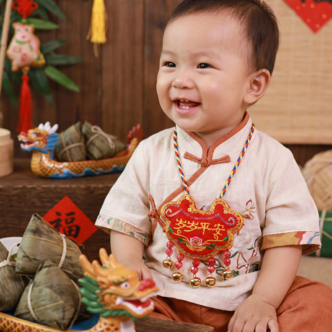 将图中的岁岁平安挂脖，挂在1岁左右宝宝的脖子上，注意挂脖的比例尺寸，高8厘米宽10厘米，端午节氛围，真实自然的照片风格，1:1正方形构图预览效果