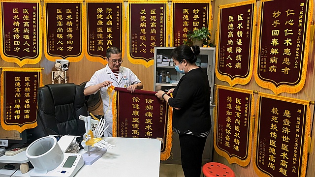 「图片1」将图中诊室面上都挂满锦旗，男性患者换成中年女性并戴口罩