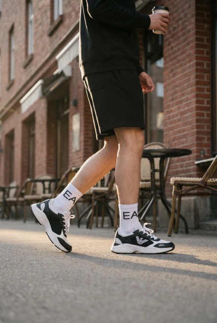 一张街头时尚风格的模特上脚运动鞋场景图，模特穿着图中这双黑白色网面老爹鞋，模特穿着白色袜子，袜子上印有字母EA，保持鞋子上原有EA7 EMPORIO ARMANI Logo文字原样不变，保持鞋子主体物预览效果