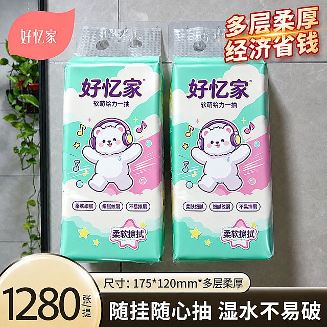 将图中悬挂的两包抽纸外包装图案完全替换为第一张白底图中的好忆家抽纸包装图案：青绿色渐变背景、白色云朵、戴耳机的白色小熊、音符星星装饰、"好忆家"品牌名、"软萌给力一抽"副标题、三个卖点标签（柔肤细腻、细腻纹湄、不易掉屑）、"柔软擦拭"字样，图案要完全贴合悬挂抽纸的包装透视和形状，保留透明挂孔结构，保持瓷砖墙面、绿植、右上角多层柔厚经济省钱字样、左下角1280张标识和底部文字信息不变，整体光影自然真实，产品立体感强