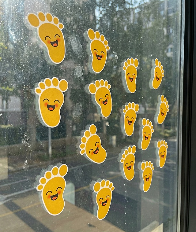 将这些脚丫贴纸打乱布局，贴在玻璃窗上，生成效果图，贴纸保持原有可爱笑脸脚丫样式，贴合玻璃窗的光影和质感