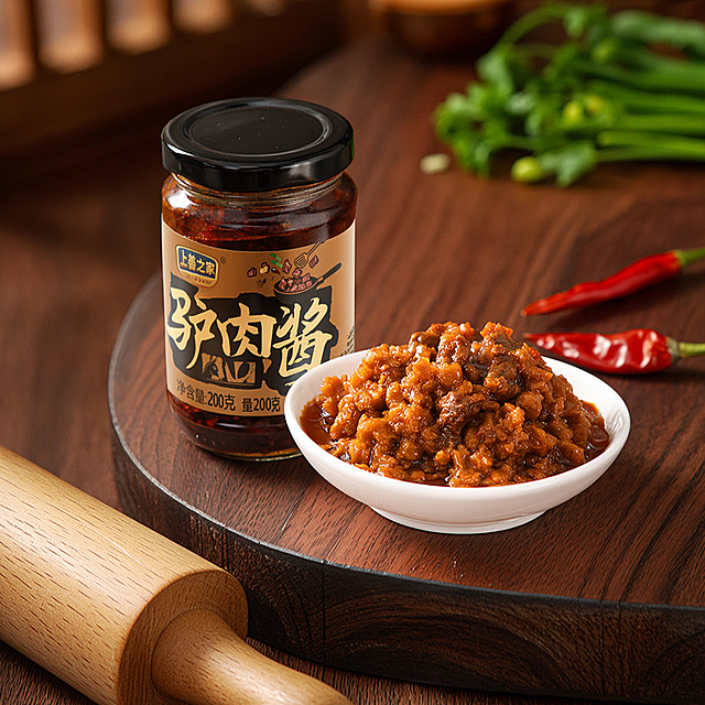 超写实美食摄影，温馨烟火气的厨房场景。
主体：驴肉酱罐头和盛放在白碗中的驴肉酱严格参照上传图片，完整保留所有可见组件、轮廓、结构、比例、材质、颜色与产品本体上的文字信息（logo/型号/规格/参数），与上传图完全一致，自然融入场景光影。保留产品主体文字，清除多余背景空白。
构图：45度俯拍，产品为第一视觉焦点，与背景在明度、色相上拉开对比，产品平稳放置在台面，符合真实重力，无悬浮感。
风格：国内电商写实风格，温馨生活化。
场景：复古木纹中式厨房台面，充满生活烟火气。
陪衬物：①台面右侧，散落两三粒新鲜干辣椒；②台面左侧，一小段干净的实木擀面杖；③背景虚化处，点缀一片绿色的葱花。
配色/材质：深胡桃木棕、米白、朱红、鲜绿；实木、陶瓷、玻璃包装材质。
光影：主光来自斜前方45度午后暖窗光，照亮产品核心展示面，整体暖调，无明显硬阴影，油润的驴肉酱呈现出诱人光泽，增强食欲感。
严格锁定宽高比为 1:1。
参数：4K写实