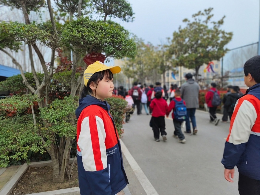 将图中女孩的黑色羽绒马甲替换为第一张图里的红白蓝拼色校服外套，保持人物、背景、图片尺寸、画质风格不变，生成高清图片预览效果