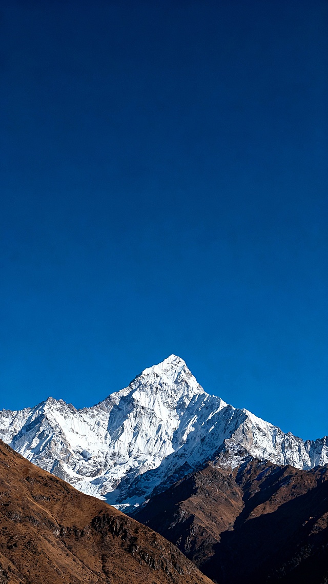 以蓝天为底，搭配巍峨的雪山与棕褐色山体，画面干净且有视觉冲击力，营造出清冷，舒展的氛围，深蓝色调，天空占画面的三分之二。
