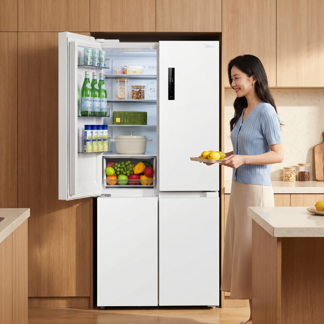 商业摄影，美的冰箱，海贝白配色，十字对开门设计，左柜门呈 90° 平开展示内部。场景为现代简约原木风厨房，浅棕色木纹柜体搭配米白色石英石台面。画面右侧站着一位气质优雅的东亚女性，身穿浅蓝色针织短袖与米预览效果