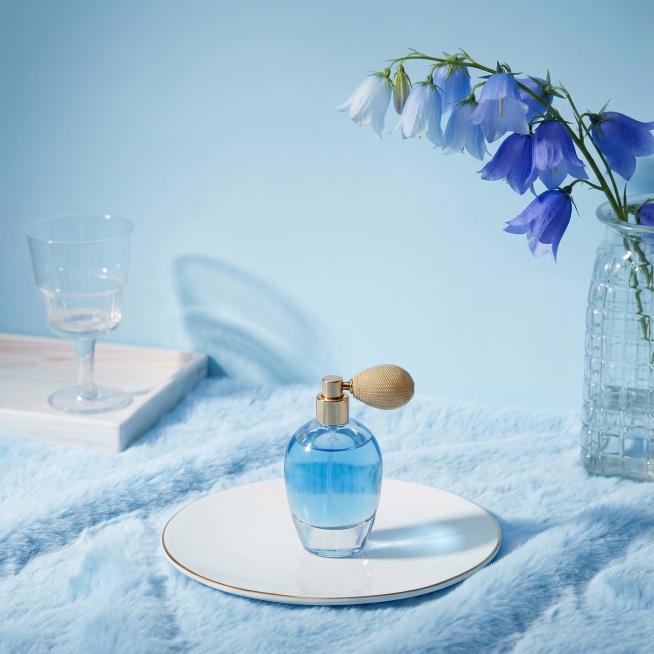 图片整体颜色改成蓝色调，花换成蓝色渐变风铃花，铺一张淡蓝色毛茸茸毯子；加一个香水瓶在圆盘中间；整体采用高清产品摄影风格，画面质感细腻、光影柔和，突出主体与舒适家居环境的融合感。预览效果