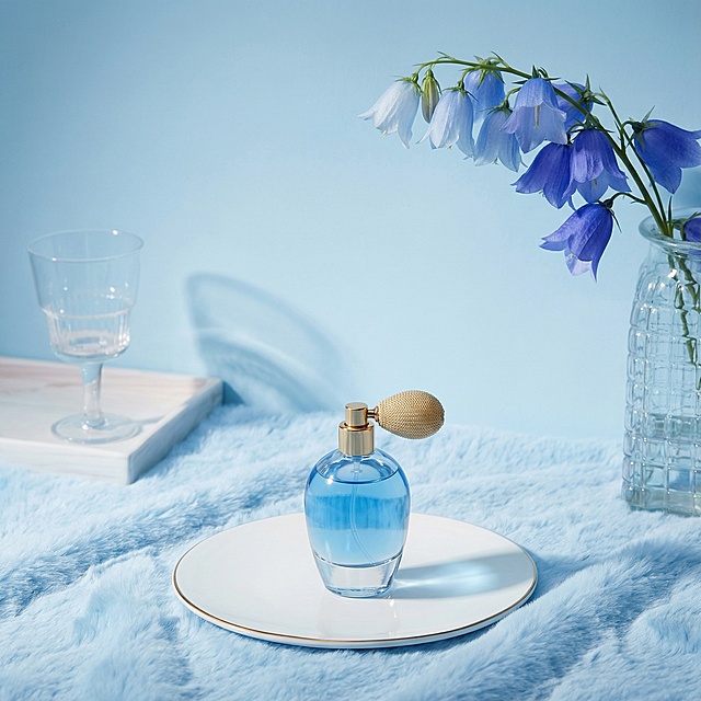 图片整体颜色改成蓝色调，花换成蓝色渐变风铃花，铺一张淡蓝色毛茸茸毯子；加一个香水瓶在圆盘中间；整体采用高清产品摄影风格，画面质感细腻、光影柔和，突出主体与舒适家居环境的融合感。