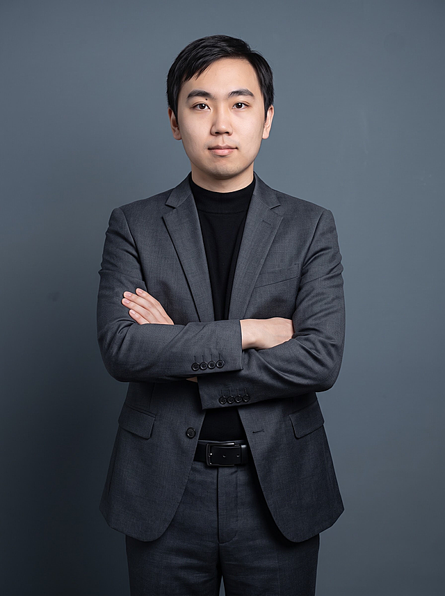 参考图中人物的脸型、发型、五官、年龄等面部特征保持一致，生成专业商务形象照。标准焦段50mm，F/4光圈（处于F/2.8-F/4区间），平视视角（镜头与人物视线齐平）；人物占画面70%，人物居中（居中构图），位于画面中心，为视觉聚焦点，入境范围头部及以下至臀部下方10cm（半身像），左右留少量背景空间，头部与画面顶部保留5%空间，头肩比例协调，人物结构准确。身穿修身精纺羊毛混纺面料的深灰色西装外套（含5%桑蚕丝提升柔光质感），平驳领（商务感正式感），左胸袋无口袋巾（简化高级感），西装下摆自然垂度；内搭黑色中领紧身针织上衣；下装精纺羊毛混纺面料的深灰色高腰直筒西裤（面料同西装）；搭配黑色哑光头层牛皮皮带（宽1.5cm），带扣为长方形拉丝黑色金属（1.8cm×2.5cm）。着装正式干练，正式严谨专业稳重，身形匀称，姿态端正，身体挺拔。呈正面抱胸的自然站立姿态：左臂搭于右臂上方，肩颈自然松弛下沉，姿态自信从容。发梢微微修整，干练大气，主体锐利。背景为简约冷调深灰色纯色背景（呈现均匀柔和质感），极简干净，背景光线均匀柔和，强化色彩对比的高级感。画质超高分辨率、细节清晰，现代精致感风格，写实摄影。肤质精细化处理，眼神直视镜头，目光坚定且澄澈，表情自然。肤质自然细腻，肤色健康均匀，哑光肤质清爽干净，保留真实皮肤细节。杰作，最佳画质，超高细节，中近景人像，皮肤质感自然清晰，柔光，正面补光，画面干净清新，高清皮肤细节；面部光比1:1.5，4800K中性光，微微修饰脸型，肤质哑光细腻，面部雾面柔光，轻透裸肌感，真实毛孔纹理。去除人物项链、耳环、包包、帽子等多余配饰。画面比例3:4。