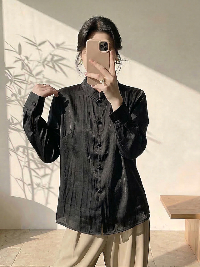 保持人物姿势、身材比例、脸型发型、暖色系新中式极简背景不变，仅将人物身上原来的衬衫替换为图片中的黑色新中式衬衫，保留这件黑色衬衫的所有细节：立领、黑色盘扣、褶皱肌理、纯色缎面面料和original版型，适配人物身体自然呈现穿着效果，光影和风格与原图保持一致，服装自然贴合身体，不改变人物整体结构和背景氛围。负向提示词：服装变形、细节丢失、颜色不对、纹理错误、比例失调、人物扭曲、水印、文字
