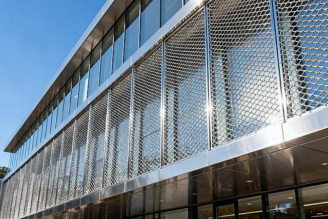 Modern commercial building facade, stainless steel chain link decorative mesh used as architectural curtain wall, uniform aperture provides good light transmission, clean lines contemporary architecture, exterior building photography, sunny weather,