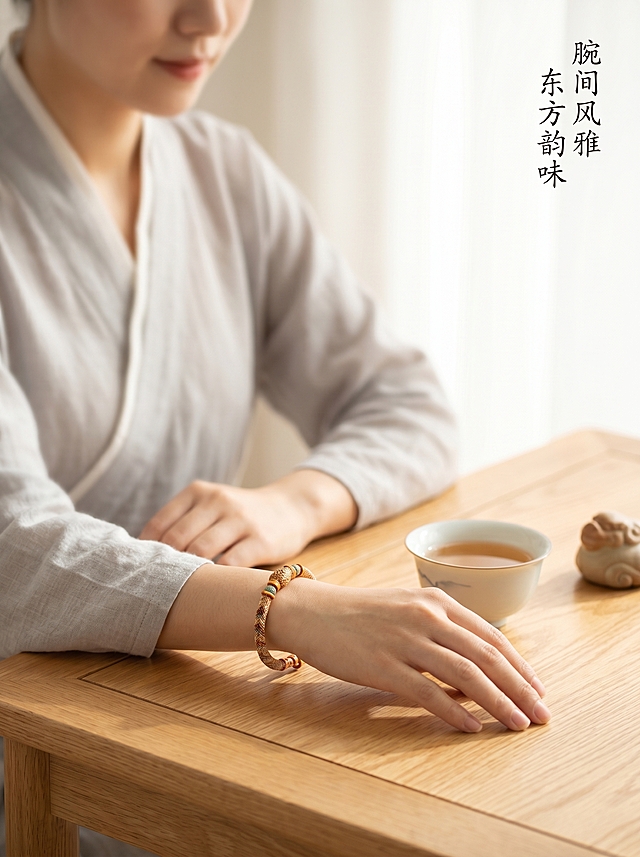 [主图 4] 场景体验展示-国风佩戴效果图。[氛围风格] 中式雅致生活场景，氛围感高级，兼具生活感。[画质] 商业摄影质感、光线自然通透、画面清晰干净，高级氛围感。[元素] 女生手腕佩戴手串，手腕自然搭在中式茶席旁边，旁边放着半盏盖碗茶杯和一片祥云茶宠，背景为浅木色茶桌，留有大量留白突出手串。女生衣着素色棉麻汉服，皮肤白皙，姿态自然放松。手串完整展示在手腕处，珠子纹理颜色清晰真实。手串为绝对视觉主体，人物虚化衬托产品。商品主体清晰，画面层次分明，空间感充足。[光影] 柔和窗边自然光，色温偏暖，突出手串温润质感，手部光影自然，场景氛围宁静雅致。[配色] 木色暖调为主，棉麻浅灰，茶水浅棕，整体配色素雅高级，符合中式审美。[视角构图] 中近景平视视角，浅景深突出手腕手串，前景虚化茶席，背景留白，空间感强。[文字版式] 右上角小文字 “腕间风雅 东方韵味”，浅色小字不遮挡主体，书法字体符合整体风格。[比例分辨率] 3:4比例，2k分辨率；文字清晰锐利，超高清。[负向提示词] 变形，水印，文字错乱，背景杂乱，遮挡手串，人脸清晰抢主体，违规文字。