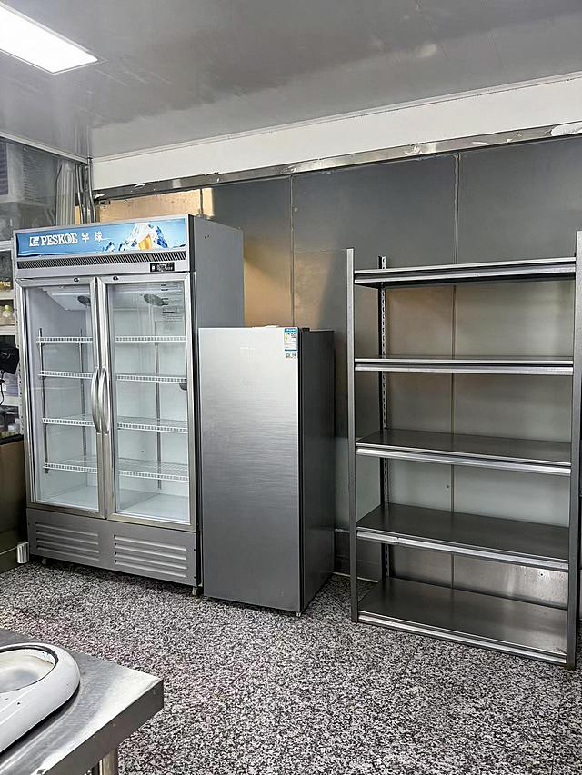 去除图片左下角的白色机器，去除右侧5层金属货架上的所有物品（包括篮子、锅、塑料盒、纸箱、包装袋等所有摆放在货架上的物品），仅保留空的货架主体结构，货架的金属框架和层板完整保留。同时将左侧双门透明玻璃展示冰箱内部的所有物品全部清空，仅保留冰箱内部的金属层架和空的内部空间，冰箱玻璃门、外观结构完全保留。严格保持房间内其他所有主体、细节、结构、颜色、光线、透视角度完全不变，不得添加或修改任何其他元素。去除物品后的区域用周围真实的墙面、地面、货架结构和冰箱内壁自然填充，光影和材质与原图一致，过渡自然无痕。最后整体提升图片清晰度，画质自然真实，保持原照片的真实感。