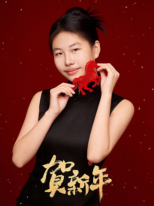 参考第一张图保留人物脸型､年龄特征生成新春时尚人像写真;喜庆温暖中式风格,高饱和中国红核心色调;标准焦段50mm,F/4光圈(F/2.8-F/4区间),平视视角(人物视线与眼部齐平),人物居中(居中构图),占画面70%,人物入境范围腰部以上区域,位于画面的中心,为绝对视觉聚焦点,大师级构图;头部发型完整,头肩比例协调;参考第二张图在画面底部的中间位置叠加金色手写狂放张扬错落感横版版式书法草书字体“贺新年”(中式感红色印章落款);人物自然优雅站姿,甜美灵动气质,嘴角温柔微笑,暖调自然白细腻通透肤质,保留自然皮肤纹理;身着深黑色哑面中式小立领无袖旗袍(面料带细腻暗纹提花1.3);身体微微向左侧微微倾,双手手指轻捻精致的传统中式纹样镂空工艺非遗马造型红色剪纸(道具),近面颊下颌处,俏皮展示状;表情自然灵动;发型为简约韩式自然高束发(发髻,自然碎发)精致发型,清透哑光妆容,淡妆,肤质白皙细腻;白皙肤质,极淡裸粉哑光眼影打底,极细内眼线填充睫毛根部,大直径深棕色带细微高光点的自然款美瞳;唇妆:微微镜面水光唇釉,唇形饱满､唇峰清晰､唇面透亮光泽;直视镜头,嘴角微微上扬轻笑,自然优雅坐姿,打光:侧前柔光(左侧散射主光),面部光影过渡自然,(面部光比1:1.3),画质为高分辨率精细质感,清晰呈现缎面纹理､镂空工艺非遗马造型红色剪纸细节;滤镜为高饱和喜庆风(强化红色系浓郁度,保留肤色自然质感);背景为酒红色哑光幕布,整体氛围古典雅致喜庆感,背景全景添加鎏金金色细碎颗粒元素;高清晰度｡去除人物之外的所有元素,滤镜:胶片颗粒感(ISO400)国风滤镜,氛围:温婉东方诗意｡