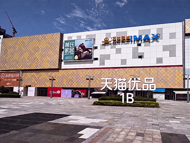 将图片里“天猫优品”整体拔高，然后把“1B”移动到“优品”两个字的正下方，保持原有的立体白色发光字效果，整体立在草坪上方，其余场景保持不变