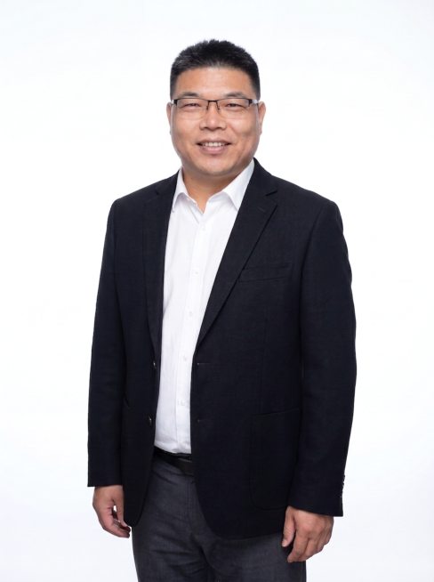 参考图修改，调整表情为自然微笑，提升气色让脸色看起来更精神健康，保持现有深色西装白衬衫穿搭、纯白背景和站姿不变，保留人物脸型发型眼镜特征，整体保持专业职业形象照风格预览效果