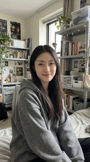 保留图片人物的面部特征，修改为这位长发女生穿着灰色宽松外套，在充满生活气息的大学宿舍，背景有置物架和各类物品，整体风格是简约日常的生活风，画面色调柔和，突出服饰的休闲感和室内的真实质感，光线还原室内的预览效果