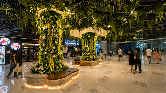 为这张商场绿植立柱场景增加亮化效果，提升绿植和休息区的灯光氛围感，保留现有的人物、座椅、绿植和场景布局，其余内容保持不变