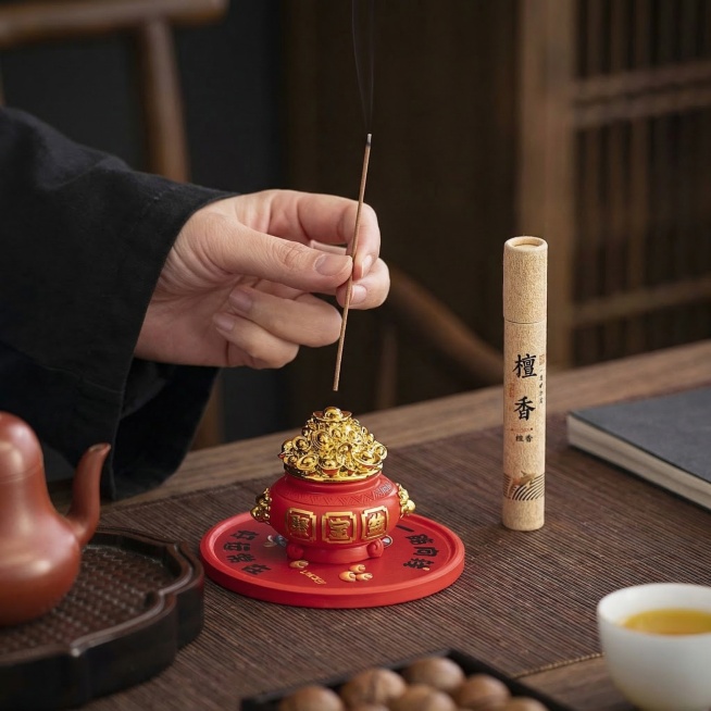 保留手、线香、聚宝盆香插、檀香、茶壶茶杯、核果所有细节和结构不变，移除多余留白，更换为统一的新中式禅意茶室深色木质茶席背景，保持产品纹理、颜色和手的姿态不变，自然柔和侧光，氛围静谧雅致，商业摄影，1:预览效果