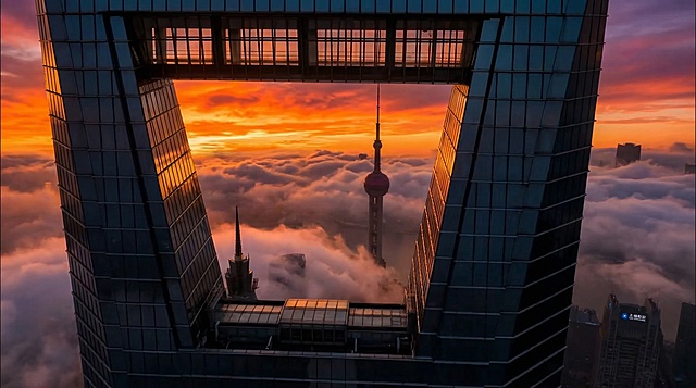 核心描述： 电影级无人机镜头，透过上海环球金融中心顶部的梯形风洞拍摄，完美框构出远处的东方明珠塔。
环境与动态： 城市下方是翻腾的云海，云雾在风洞口缓缓流动。
光影与色彩： 燃烧般的火红日落，天空呈现浓烈的橙色和紫色。前景建筑呈现剪影效果，玻璃幕墙边缘反射着金色的余晖。
质感： 赛博朋克氛围，高对比度，超高清，8k分辨率，史诗感。