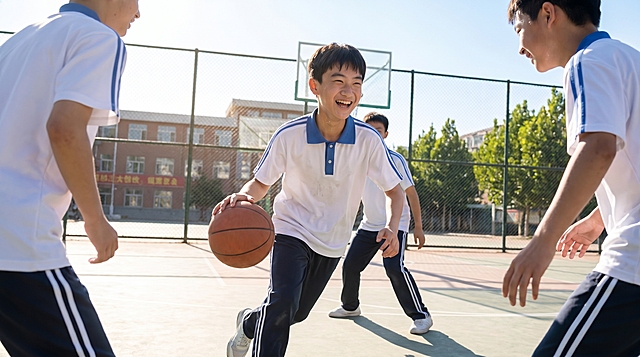 同一个穿蓝白校服的初中男生，在操场上和同学尽情地打篮球，脸上洋溢着灿烂的笑容，阳光明媚的户外操场，写实风格，16:9尺寸