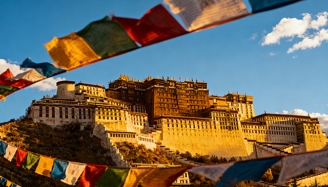 专业旅行摄影风格的西藏布达拉宫，金色阳光照射在建筑上，天空是澄澈的蓝天白云，色彩鲜艳的经幡在风中飘扬，画面通透有质感，超高清细节丰富，真实自然的旅行风光