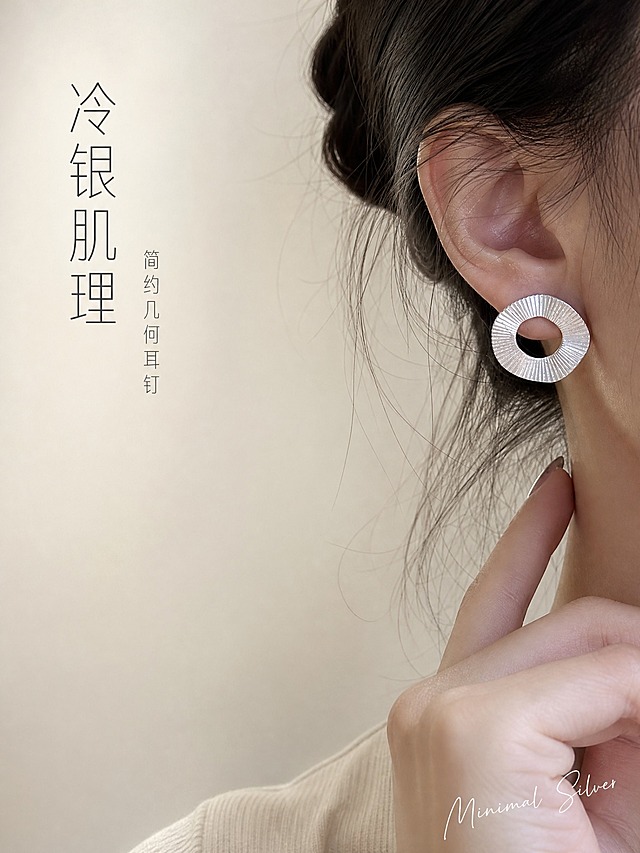[主图-1] 银色肌理圆环耳钉 首图点击率 佩戴大片。
[统一基调] 高级冷银轻奢风格，奶油米白渐变背景，柔光箱高光+窄条轮廓光体现金属质感，标题字色深炭灰，辅助字色中暖灰，强调色冷银白，字体为现代纤细无衬线体，整体克制精致。
[画面] 亚洲女性右耳侧佩戴特写，银色肌理圆环耳钉居中偏右，主体占比约40%，耳侧肌肤细腻，发丝自然散落几缕，手指轻触下颌线，侧脸轮廓柔和，背景为纯净奶油米白渐变，左侧留白。耳钉保持原图造型：不规则圆环、放射状拉丝肌理、哑光银色金属质感，结构与比例完全一致。
[光影质感] 左前侧柔光主光，右侧银色耳钉边缘有清晰轮廓光，金属表面有细腻拉丝纹理反光，肌肤通透自然，阴影柔和不生硬，珠宝级精修质感。
[配色] 背景奶油米白渐变，耳钉冷银色，肌肤暖米色，文字深炭灰。
[文字版式] 左上角竖排两行纤细文案，主标题"冷银肌理"字号较大，副标题"简约几何耳钉"字号缩小50%以上，右下角小号手写体英文装饰"Minimal Silver"，文字不遮挡耳钉主体。
[输出要求] 比例3:4竖版，2K高清，耳钉清晰锐利，金属质感真实，文字清晰可读。负向：变形、错字、模糊、杂乱背景、水印、平台Logo、廉价塑料感、手指畸形、面部扭曲。