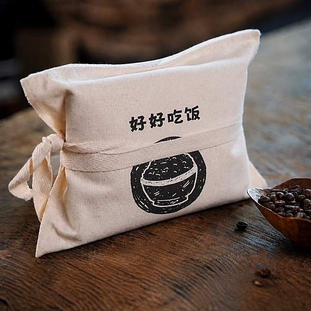 去掉米白色布包上的两条白色纸封条（标签），修复封条遮挡的区域，使布包的米白色帆布质感自然完整。然后在布包正面中央位置印上黑色的图案：上方是"好好吃饭"四个黑色粗体字，下方是一个黑色圆形印章风格的一碗米饭图案（黑白版画风格），图案贴合布包的曲面透视，像是印在帆布上的效果。保持画面其他部分不变，包括布包的绑带、咖啡豆、木勺、木质桌面、整体光影和氛围。高清画质，商业摄影质感。