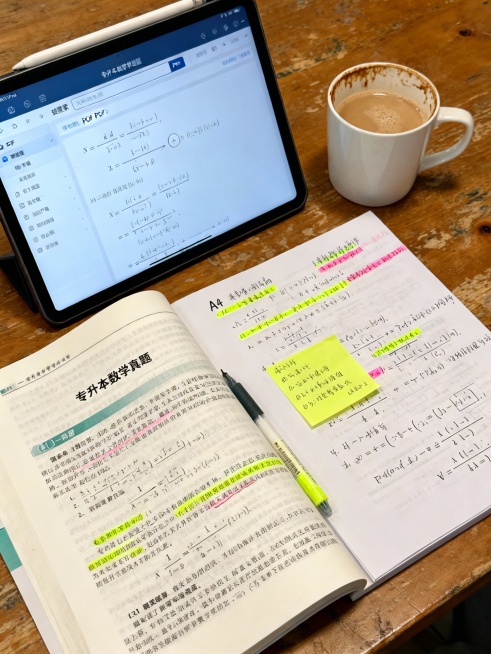 书桌一角，摊开的练习册、iPad（显示电子版公式PDF）、旁边放着打印装订好的手抄版重点公式册，上面用荧光笔画着重点。一杯提神饮品入镜，氛围专注。

AI指令：真实摄影风格，俯拍视角。一张大学生书桌，预览效果
