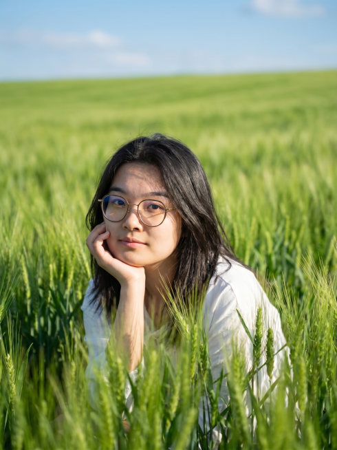 根据这张人像图生成艺术照，背景替换为绿色的麦田，保留人物样貌特征，整体风格自然清新预览效果