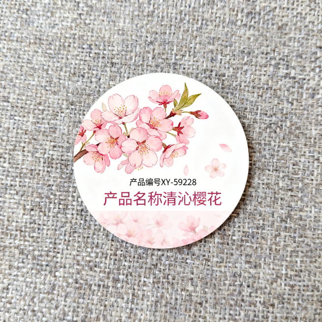 圆形产品标签，清新樱花主题设计，整体为正圆形，画面包含自然绽放的粉嫩樱花，图案和清沁樱花主题呼应，清晰标注文字：产品编号"XY-59228"，产品名称"清沁樱花"，设计清新精致，适合作为产品标签使用预览效果