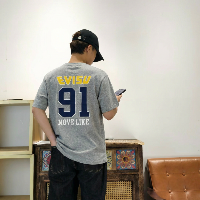 让图中人物穿上第二张图片里的那件灰色衣服，保持衣服原本的颜色和上面的文字图案不变，保留人物原本的姿势、帽子、裤子和背景不变预览效果